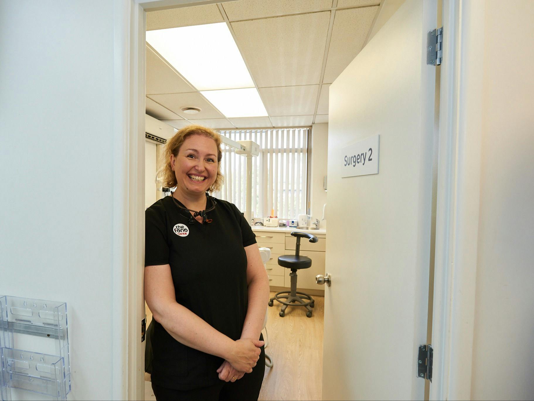 photo of smiling female in dental uniform standing by consult room